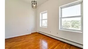 Una habitación con suelo de madera, paredes blancas y dos ventanas.