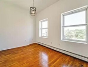 A room with hardwood flooring, white walls, and two windows.