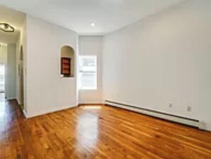 A room with hardwood flooring, white walls, and a small window.