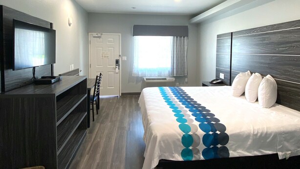 Une chambre d’hôtel moderne avec un grand lit, un téléviseur posé sur une console en bois, un bureau et une fenêtre avec des rideaux.