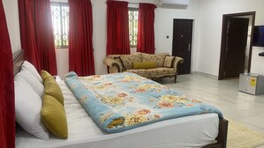 Een hotelkamer met een bed, een bank, rode gordijnen, een airconditioningsapparaat en een televisie.
