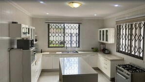 Een moderne keuken met witte kasten, een centraal eiland, een kookplaat en een raam met decoratieve roede.