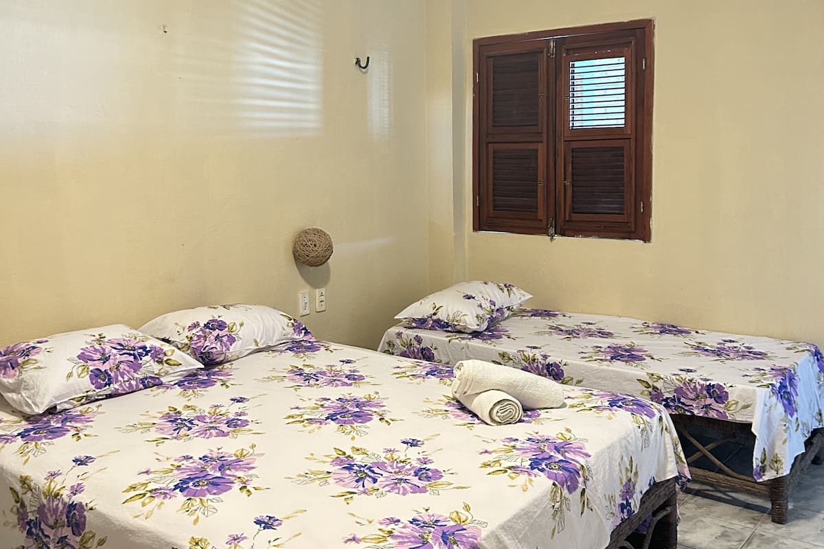 Quarto com duas camas, cada uma com roupa de cama floral, uma porta de madeira e um ar condicionado na parede.