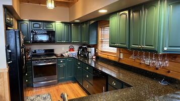 A kitchen with green cabinets, a black refrigerator, a stove, a microwave, and a coffee maker.