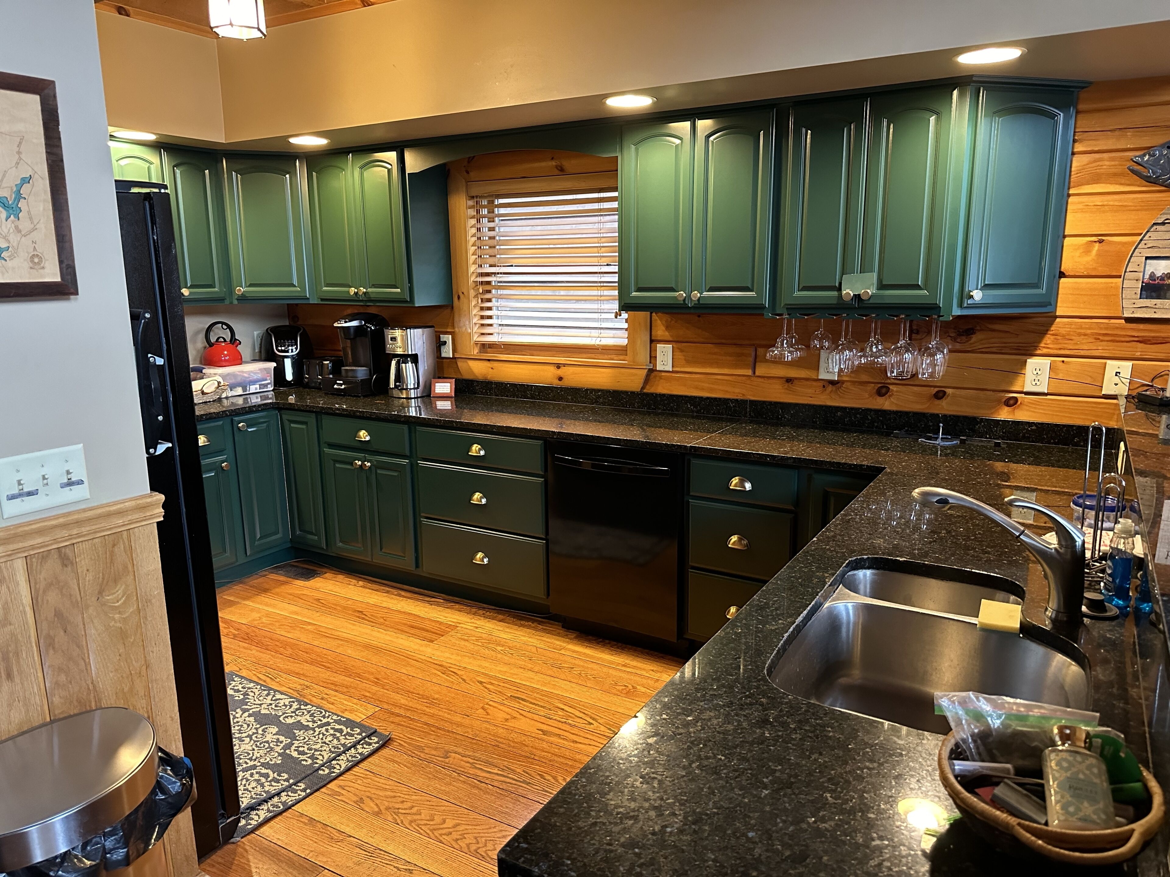 A kitchen with green cabinets, a black countertop, and a stainless steel sink.