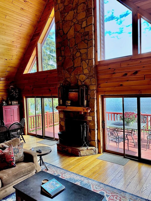 A spacious living room with a stone fireplace, large windows, and a view of the outdoors.