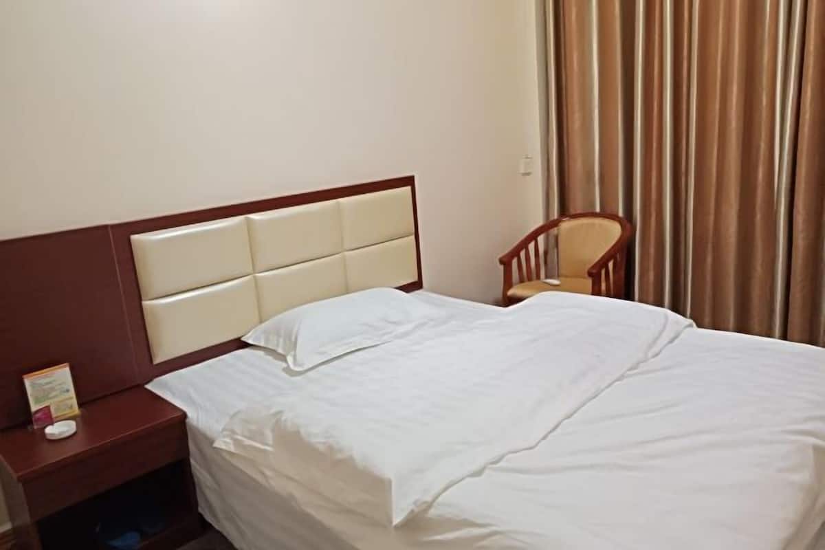 A hotel room with a bed, a nightstand, a chair, and a curtain.