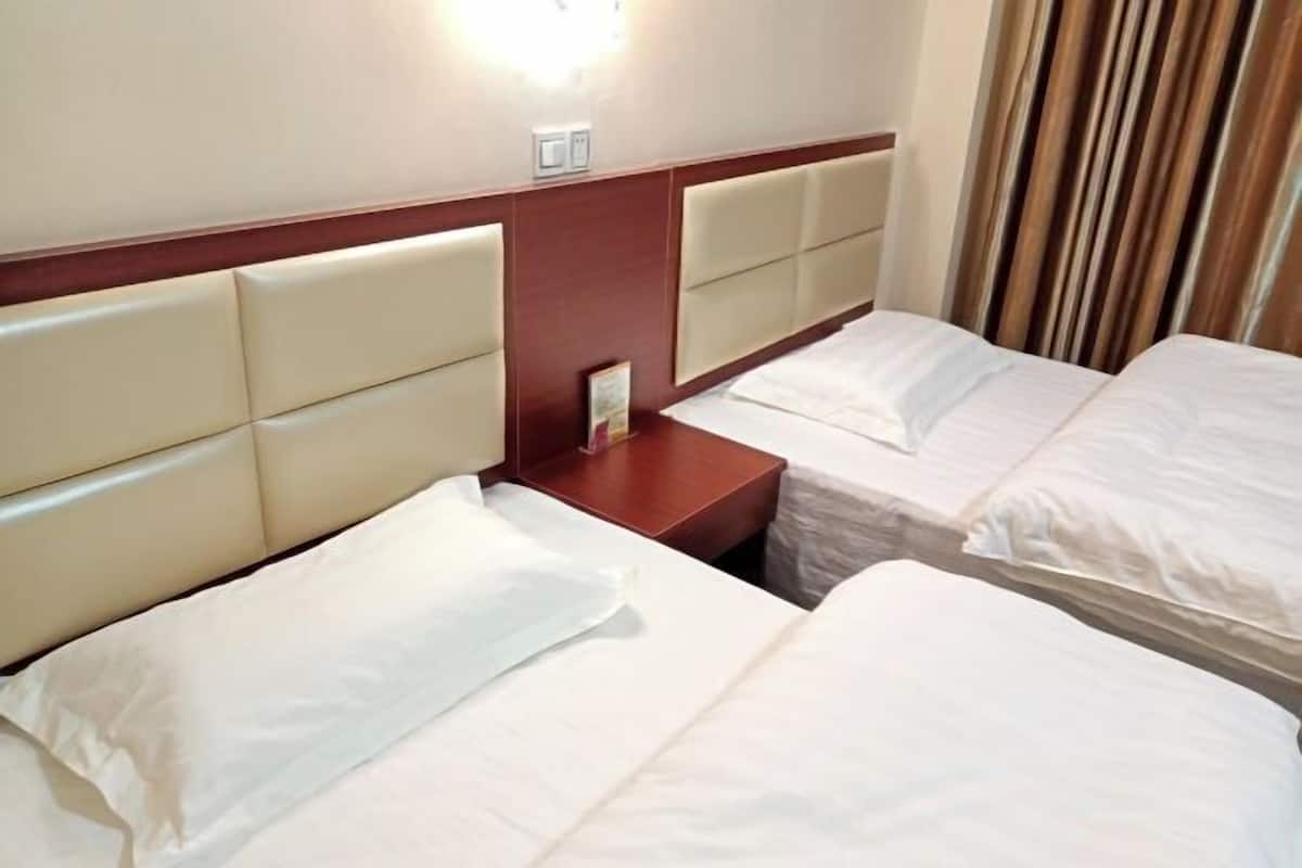 A hotel room with two beds, a wooden nightstand, and a wall-mounted light fixture.