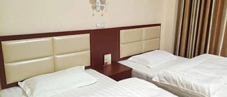 A hotel room with two beds, a wooden headboard, a nightstand, and a wall-mounted lamp.