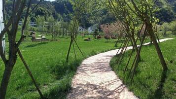 A gravel path in a green area with trees and a building in the background.