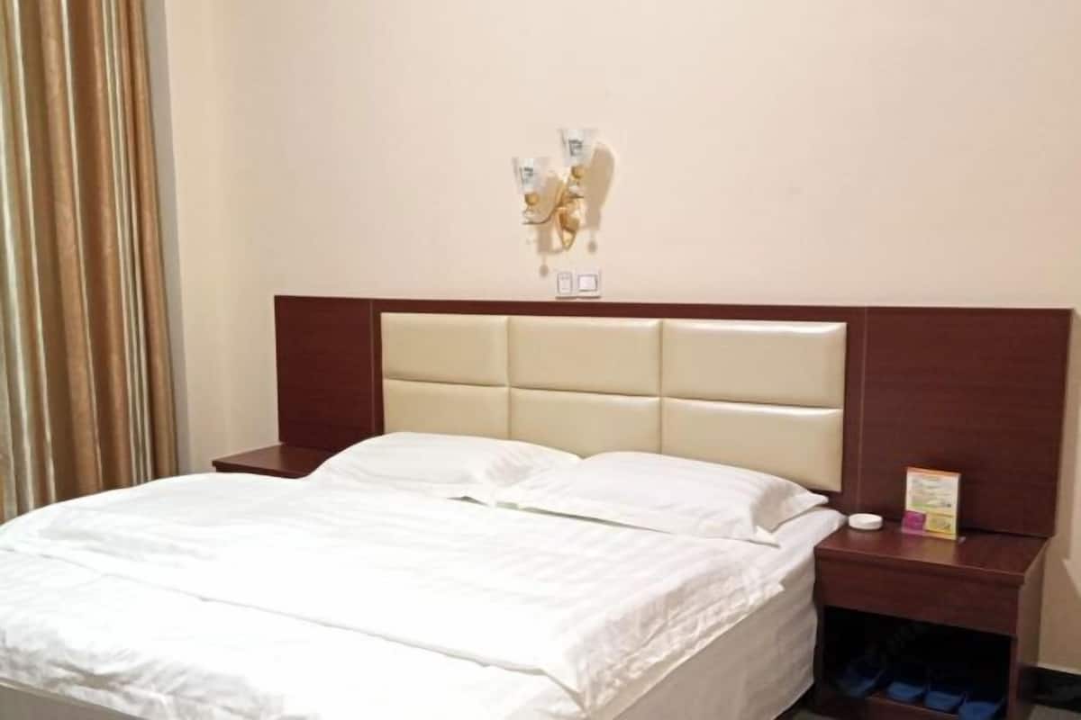 A hotel room with a bed, a nightstand, a wall-mounted light fixture, and a curtain.