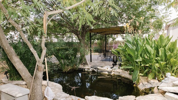 Un jardín con un estanque, zona de estar y un pérgola.