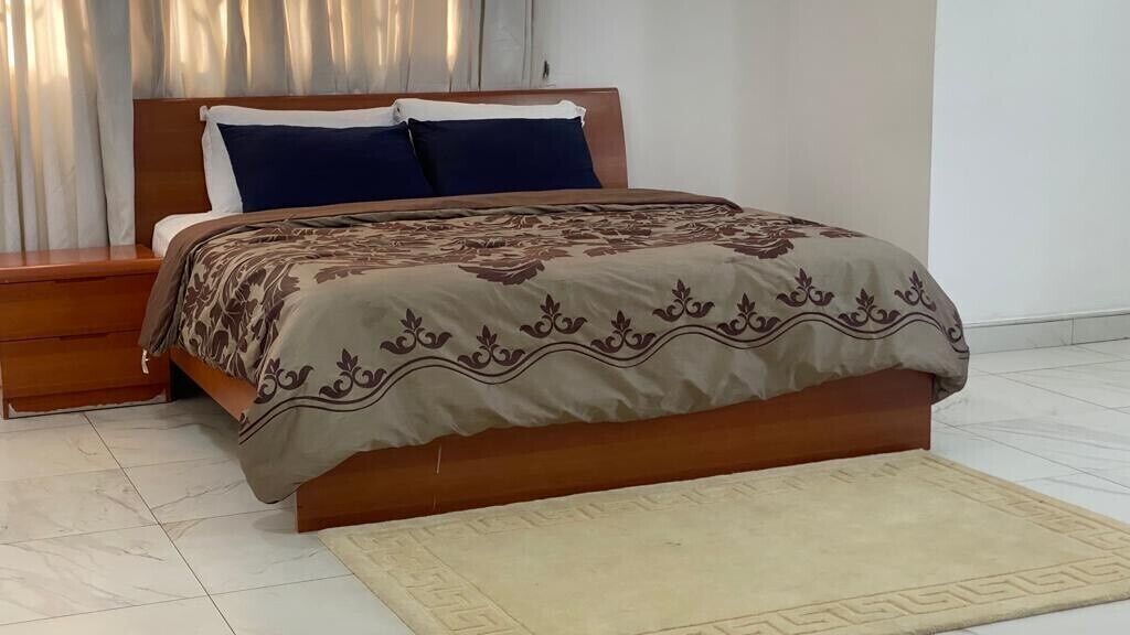 A neatly made bed with a patterned bedspread, a wooden headboard, and a matching wooden nightstand.