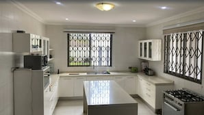 Une cuisine moderne avec des meubles blancs, un îlot central, une cuisinière et une fenêtre ornée de barreaux décoratifs.