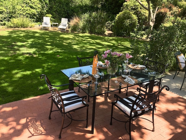 Enjoy dining al fresco with a table set for four, surrounded by lush greenery and trees.