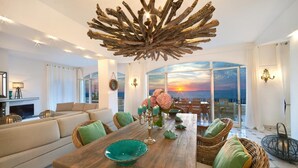 A spacious living room with a large wooden dining table, comfortable seating, and a view of the sunset over the sea. - Villa dei Sogni in Massa Lubrense (Massa Lubrense)