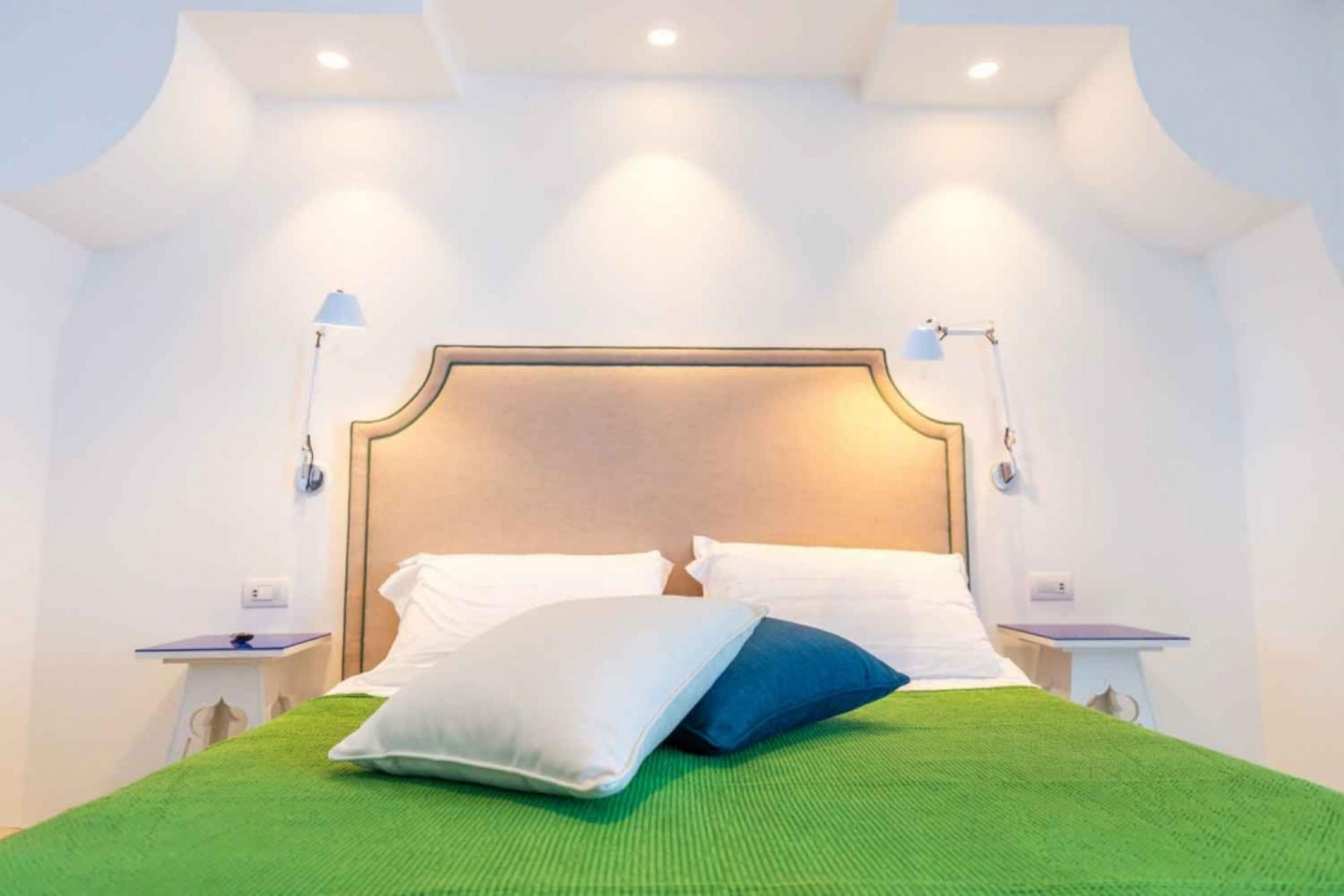 A neatly made bed with a green bedspread and two pillows, a wooden headboard, and two bedside lamps.