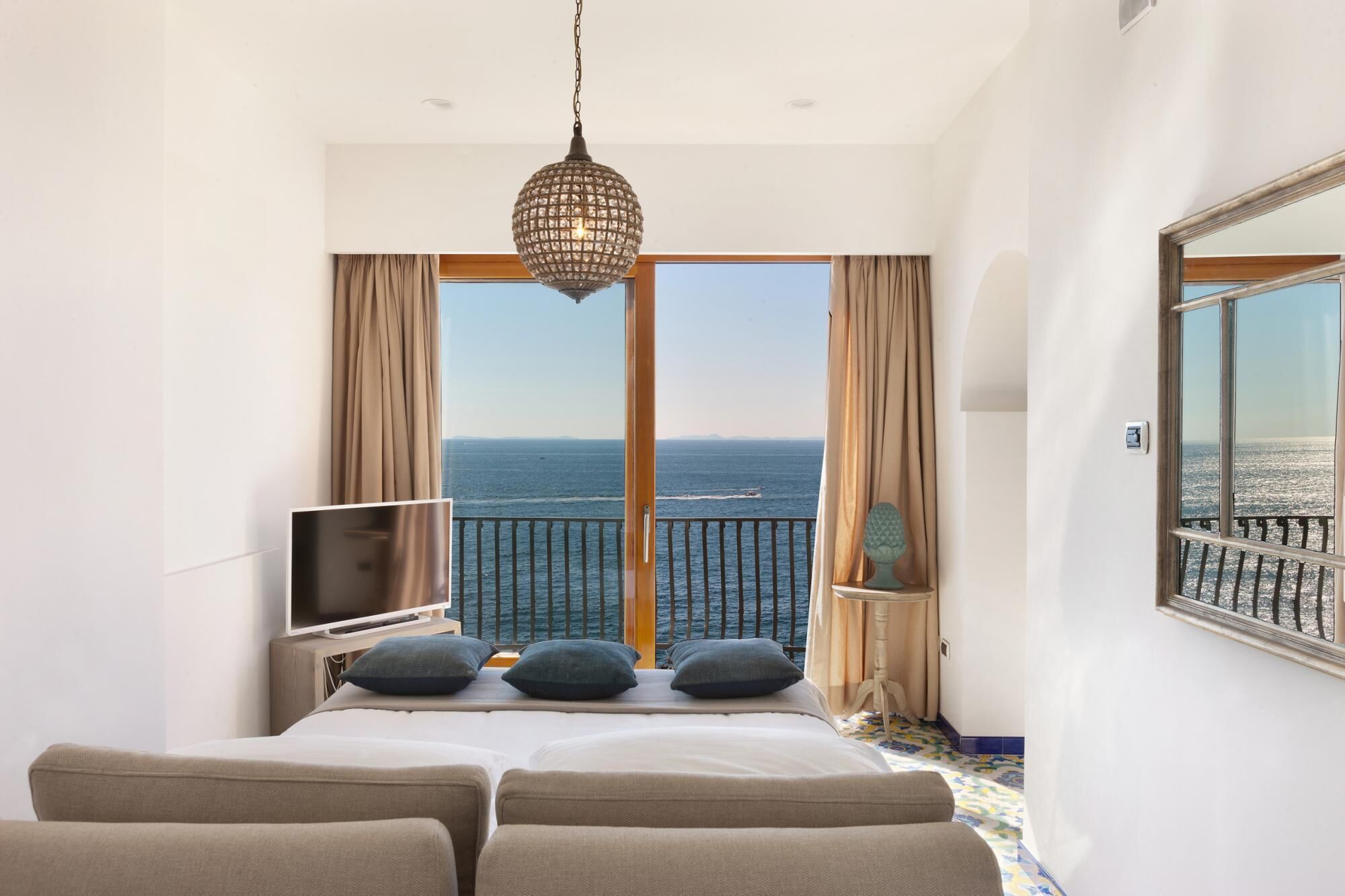 A hotel room with a bed, a TV, and a balcony with a view of the sea.