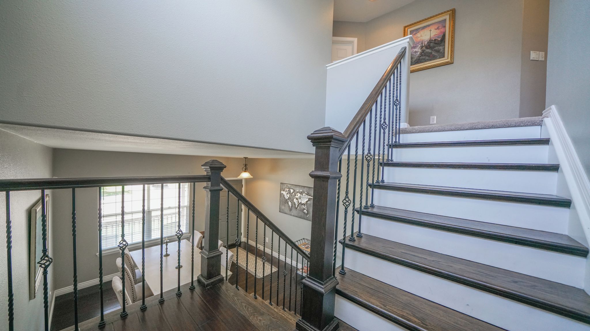 A staircase with a dark wooden handrail and balusters, leading to a landing with a light fixture and a framed picture.