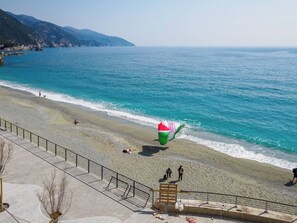 A beach with a large inflatable structure, a paved walkway, and a view of the sea and distant hills.