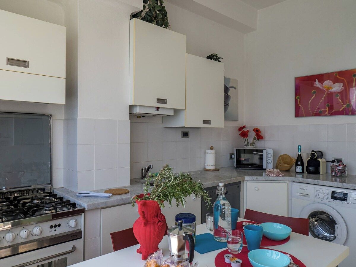 Une cuisine moderne avec des meubles blancs, une cuisinière à gaz, un four à micro-ondes, un lave-linge et un coin repas avec une table mise pour deux personnes.
