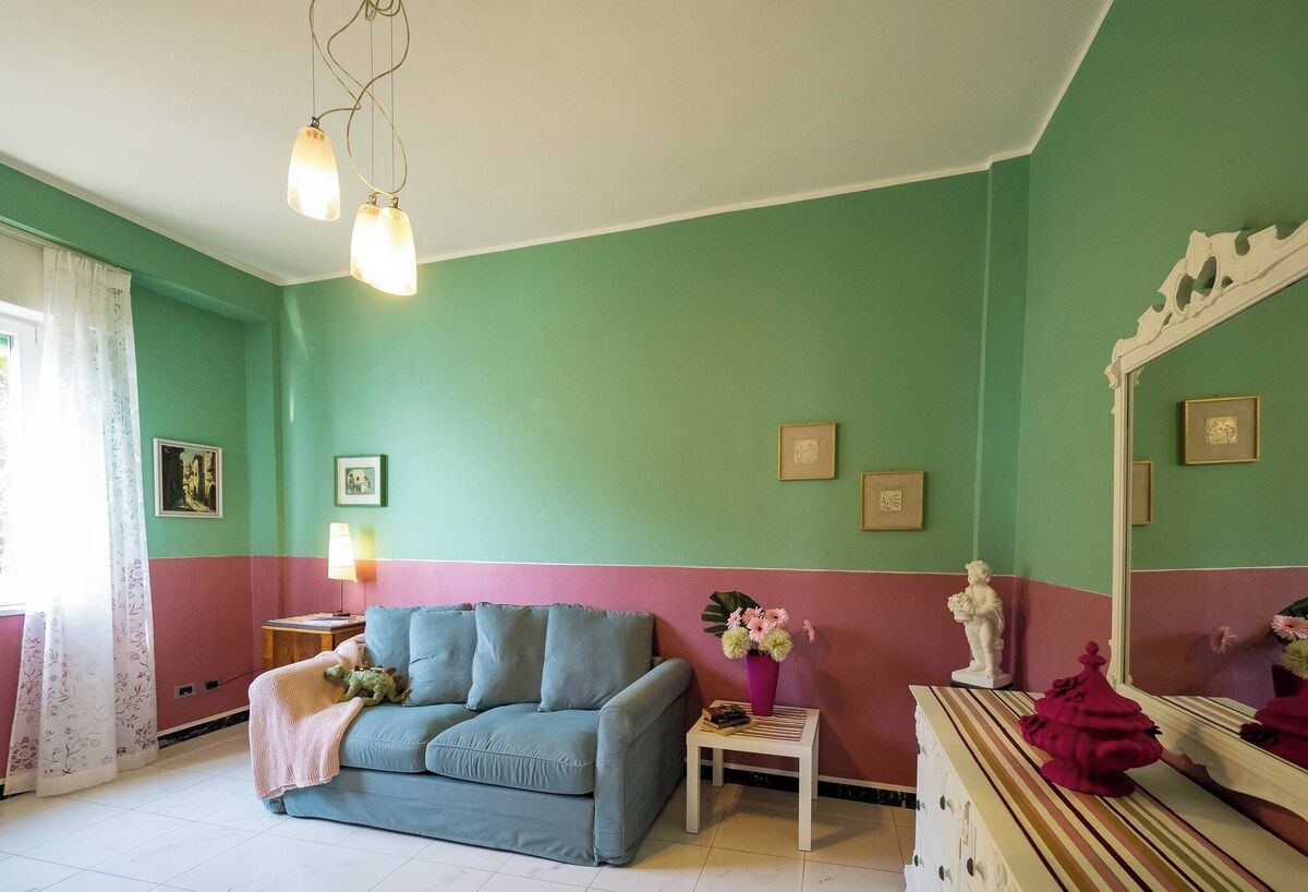 Ett rum med en grön och rosa vägg, en soffa, ett litet bord med en lampa och en spegel.