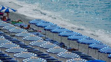 A beach with rows of blue and white striped umbrellas and lounge chairs.