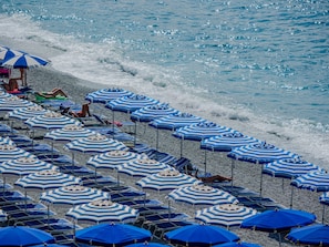 A beach with rows of blue and white striped umbrellas and lounge chairs.