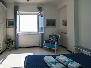 A bedroom with a bed, a chair, a radiator, and a window with curtains.