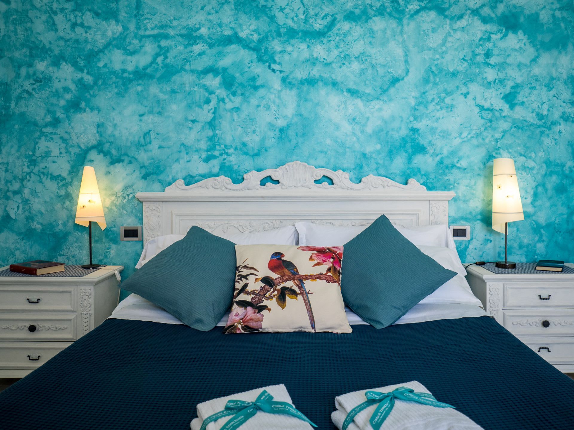 Un lit avec une tête de lit blanche, deux oreillers, une couvre-lit bleue et deux lampes de chevet.