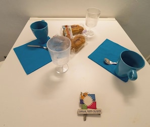 A table with a blue napkin, a blue mug, a clear glass, a spoon, and a small card with text. - Picagetta Tiny Room with AC (Vernazza)