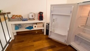 A kitchen with a refrigerator, wooden floor, and a shelf with kitchen items.