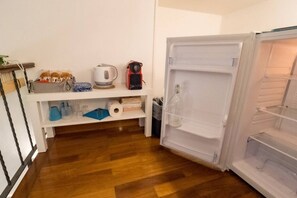 Una cocina con refrigerador, piso de madera y un estante con utensilios de cocina.