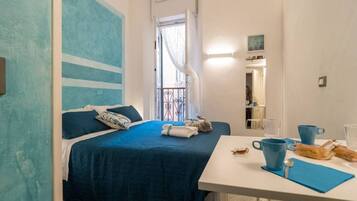 Una camera da letto con un letto, un tavolo e una sedia, una finestra con tende e un quadro appeso al muro.