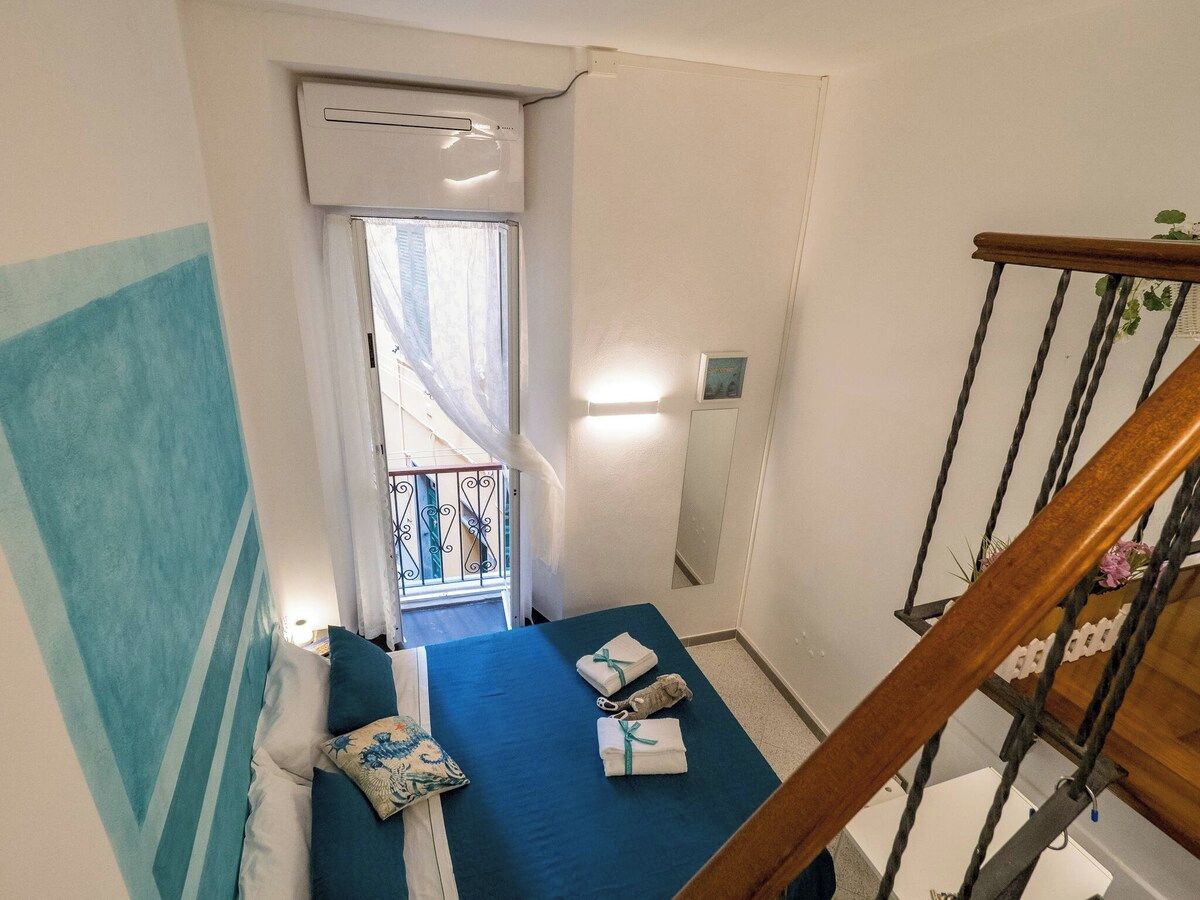 A narrow room with a bed, a window, and a staircase.