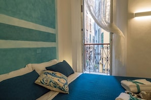 A bedroom with a bed, pillows, a view of the street through a balcony with a metal railing.
