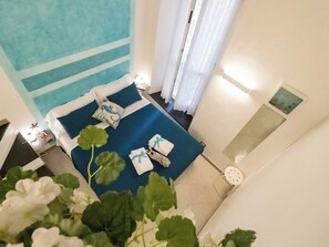 A hotel room with a bed, a nightstand, a window with curtains, and a wall-mounted clock. - Picagetta Tiny Room with AC (Vernazza)