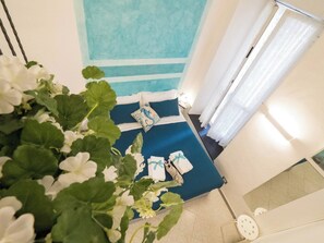 A hotel room with a bed, a window with curtains, and a plant with white flowers.