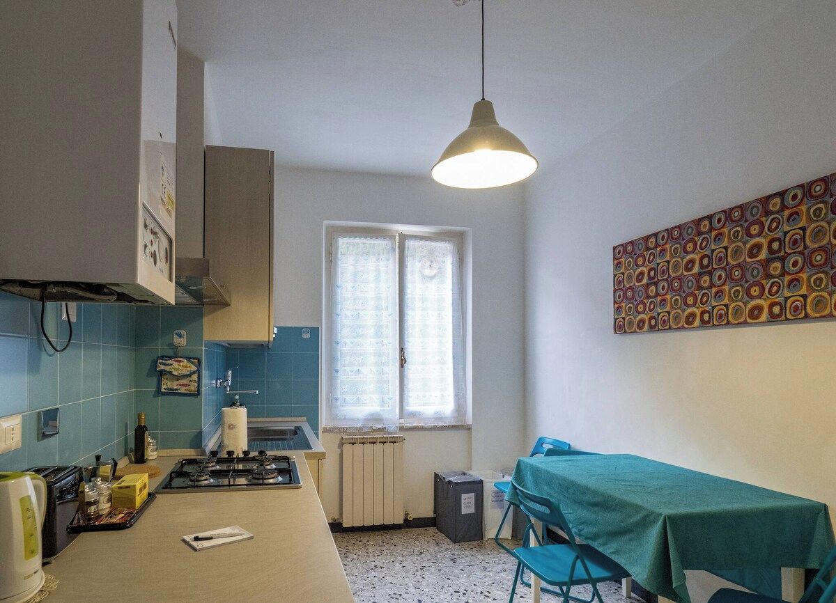 Une cuisine équipée d’une cuisinière à gaz, d’un évier et d’une fenêtre avec des stores.
