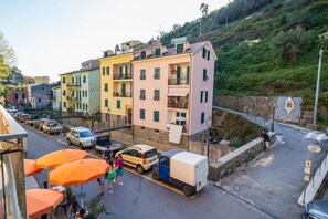 Une vue d’une rue d’un quartier résidentiel, avec des bâtiments aux couleurs vives, des voitures garées et quelques personnes qui se promènent.