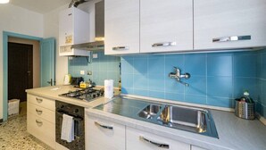 Een moderne keuken met witte kasten, een blauwe spatwand, een roestvrijstalen spoelbak en een gasfornuis.