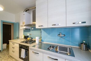 Una cocina moderna con armarios blancos, salpicadero azul, pileta de acero inoxidable y estufa a gas.