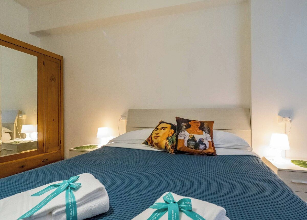 Ein Hotelzimmer mit einem Bett, zwei Kissen, einem Nachttisch mit Lampe, einem Spiegel und einer blauen Bettdecke.