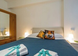 A hotel room with a bed, two pillows, a nightstand with a lamp, a mirror, and a blue bedspread. - La Casa di Frida Family Apartment (Vernazza)