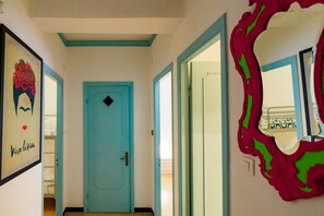 Un pasillo con una puerta turquesa, un espejo de marco rojo y un cuadro colgado en la pared.