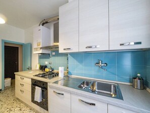 Une cuisine équipée d’une cuisinière à gaz, d’un évier en acier inoxydable et d’un dosseret de carrelage bleu.