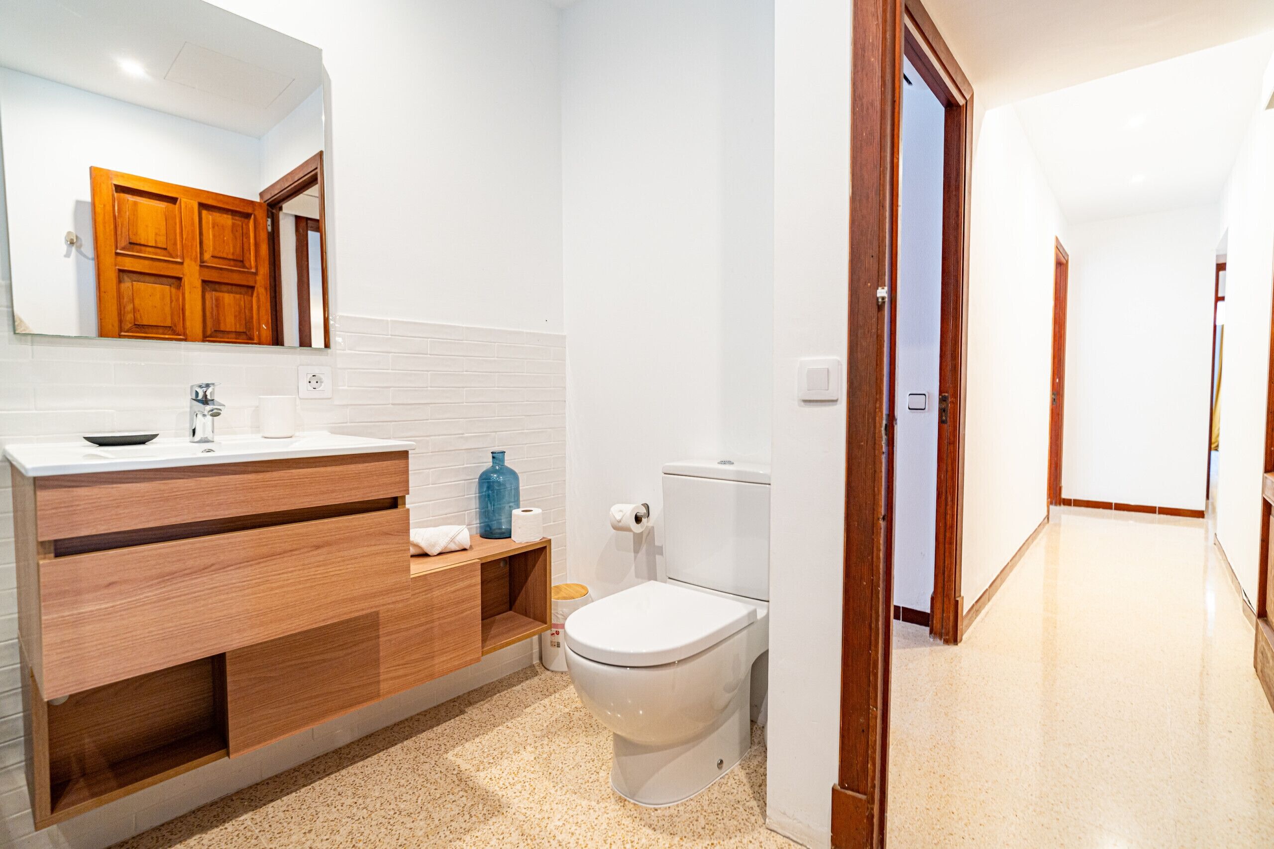 A modern bathroom with a wooden vanity, white toilet, and a mirror above the sink.