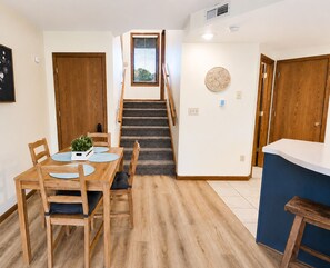 A dining area with a wooden table and chairs, a staircase, and a wall-mounted decorative plate. - Cute & Cozy King Suite Villa ~ Near Golf, Trails, Spa (Galena)