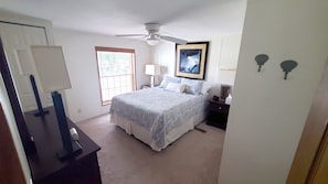 Une chambre à coucher avec un lit, un ventilateur de plafond, une fenêtre, une table de chevet et une lampe.