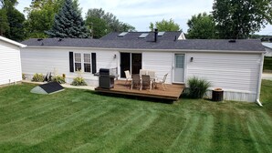 A single-story mobile home with a deck, outdoor seating, and a small garden area. - Silver Lake - 4th of July - Lake Access - MIS (Addison)